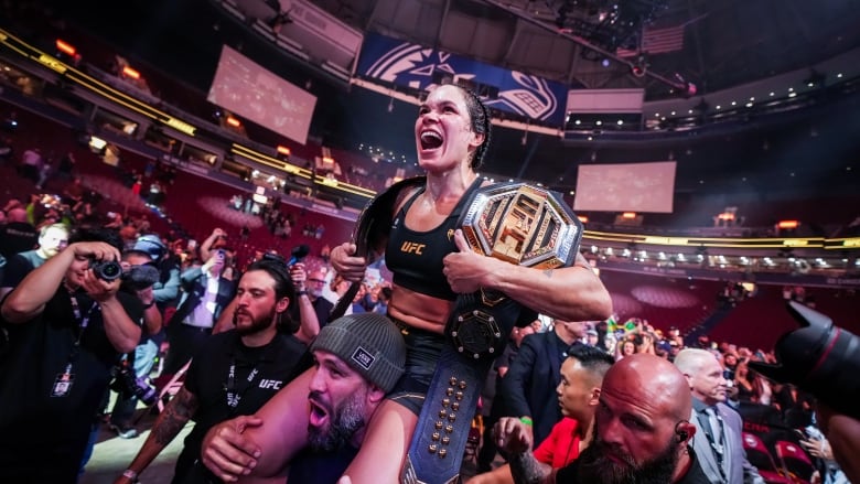 Amanda Nunes wears UFC attire as she celebrates on the shoulders of a man wearing a toque. 