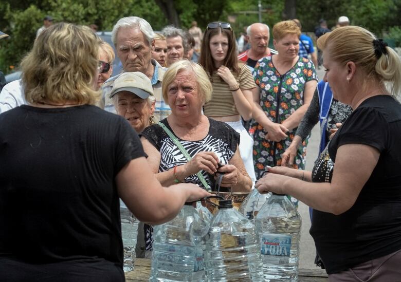 A small group of people gather near a table with large plastic water bottles on it.