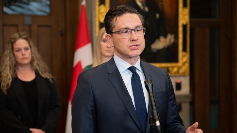 A man speaks at a microphone, in front of two women.