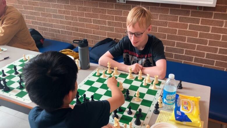 Louis sits with a friend at a table with a chess board between them. 