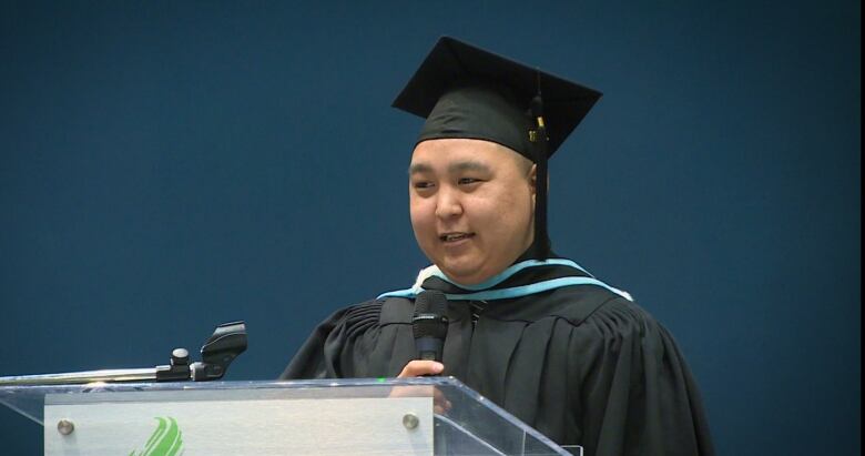 a man in graduation cap and gown at a podium