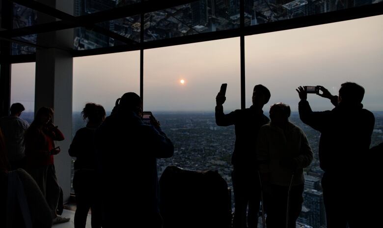 People standing inside a tower take pictures through the windows of the setting sun blanketed in haze from wildfires.