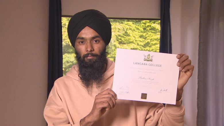 A man in a turban and full beard holds up a diploma from Langara College.