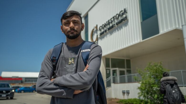 A young man stands in front of a college.