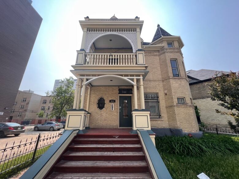 An ornate, three storey brick house with stairs leading up to a front porch, and a balcony above, is shown in this picture.