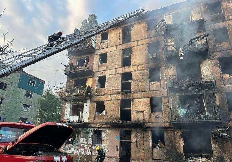 A man climbs on a rescue ladder to a burned out brick building.