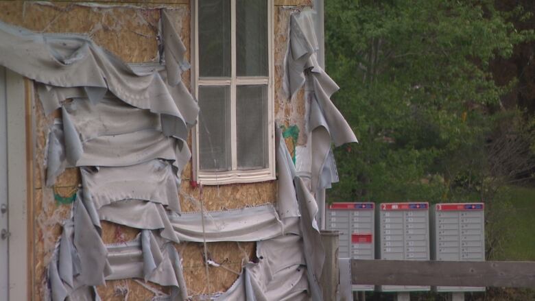 Strips of drooping vinyl siding hang from the side of a building.