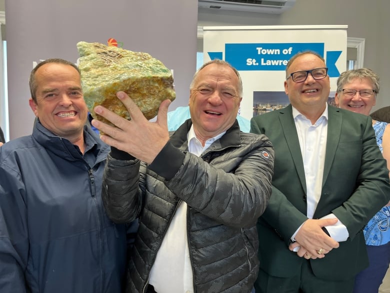 a man holds up a chunk of fluorspar and smiles.