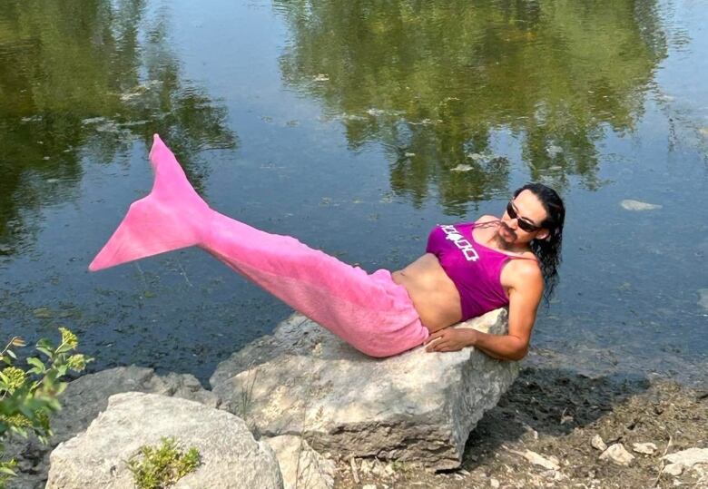 A man lies on a rock in a merman costume with a big pink fin and a pink Six Nations bra.