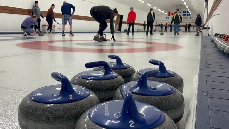 Curling stones in the foreground, curlers in the background.