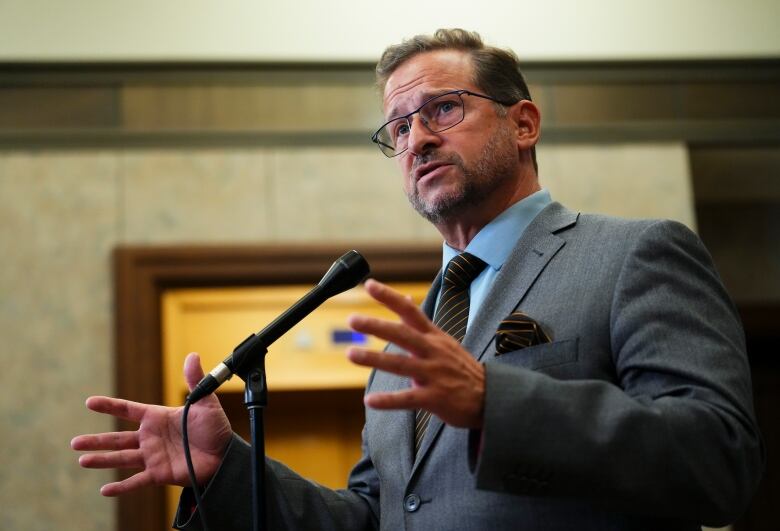 A man in a grey suit speaks to reporters outside the House of Commons.