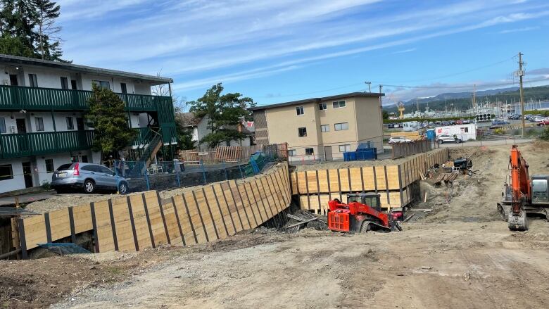 Next to a construction site, a parking lot has collapsed and taken trash bins and a car with it.