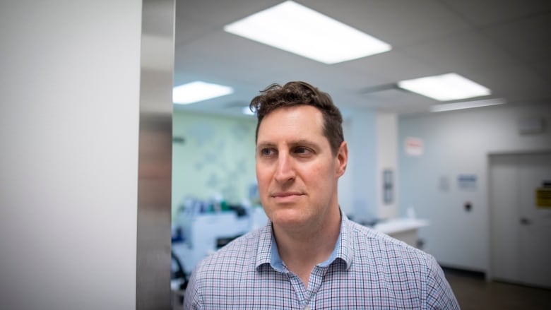 A white man in a blue, purple and white checked shirt stands in an empty medical lab.