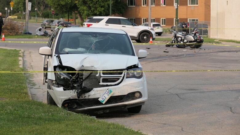 A minivan with a smashed front end is in the foreground. A motorcycle sits broken in the background.