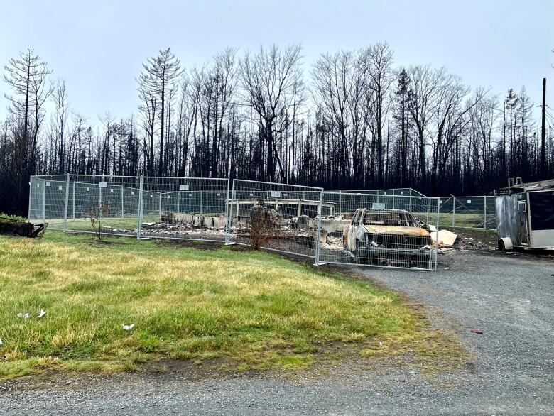 Fencing surrounds a burnt property and truck, with black trees in the background.