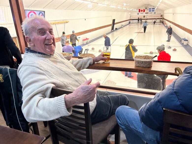 A smiling older man sits overlooking a curling sheet.