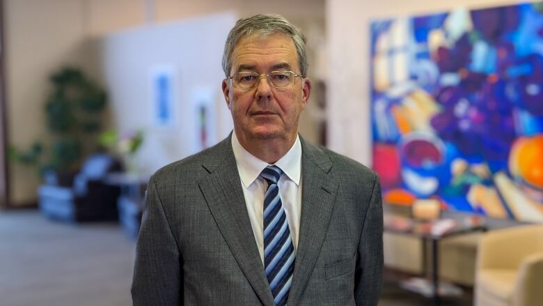 Man in business suit stands in front of colourful painting. 