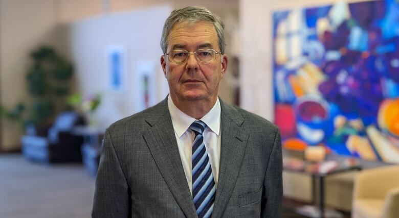 Man in business suit stands in front of colourful painting. 