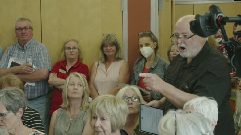 A man points and speaks forcefully within a crowd.