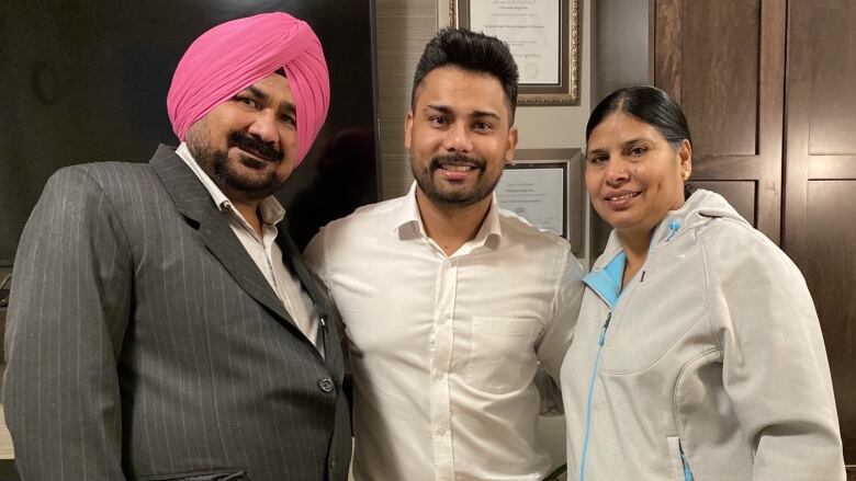 A man and his parents, standing on either side of him, smile at the camera