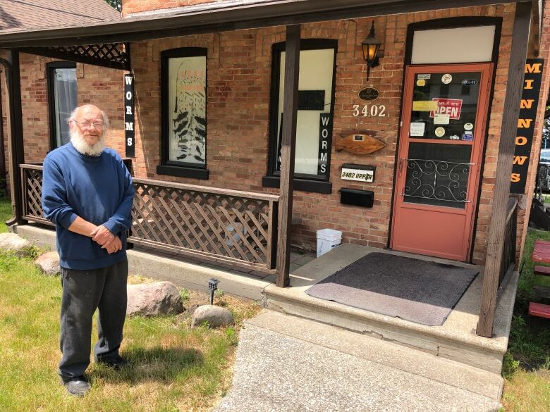 A bearded man stands outside of a fishing shop with a sign that says it is closed. 