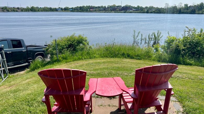 Two empty, red beach chairs are seen overlooking a lake