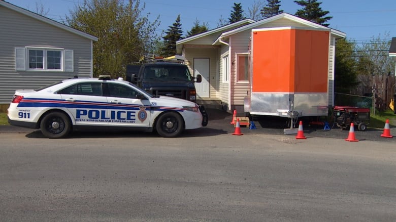 A police car and an orange trailer sit parked in front of a house.