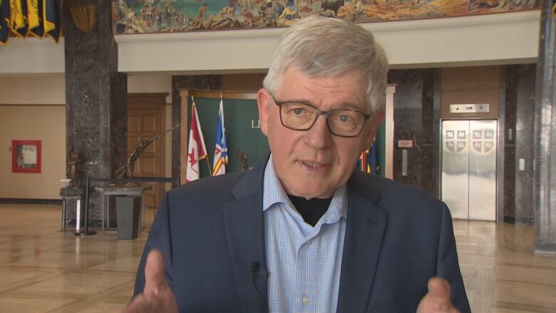 A man wearing a blue blazer and glasses stands in the lobby of Confederation Building.