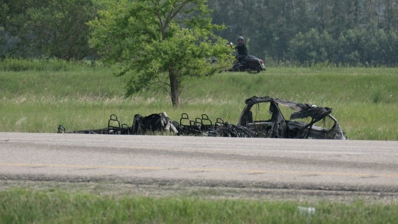 A vehicle in a ditch. The top is burned off and the seats inside are visible.