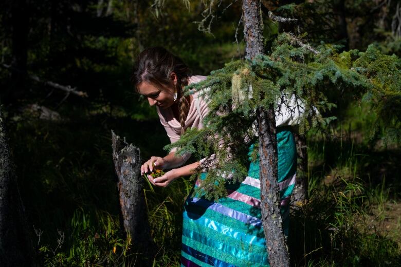 A women holds some vegetation as she crouches in the forest.