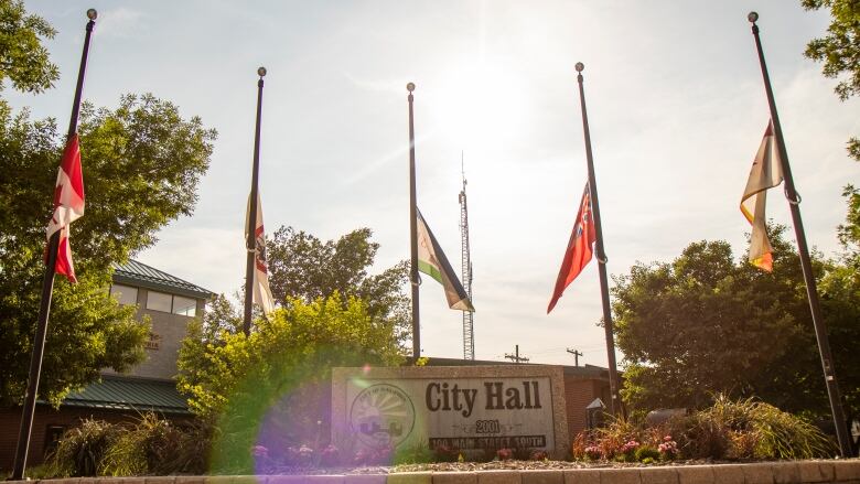 Green trees and flagpoles, with the flags at half-mast.