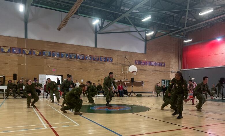 A group of people dressed in green camouflage dance in a gym. 