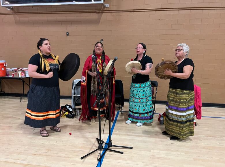 A group of women holding drums stand around a microphone.