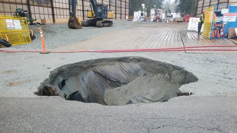 A medium-sized hole, set off by orange cones, in seen in the pavement of a city street.