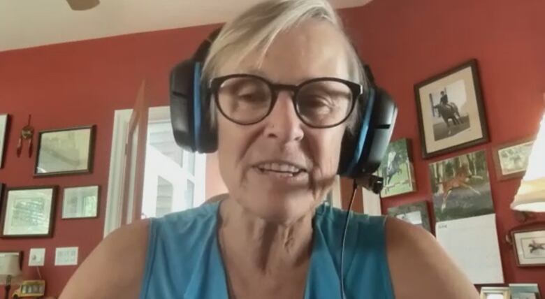 Woman with short white hair wearing headphones looks into webcam while talking.