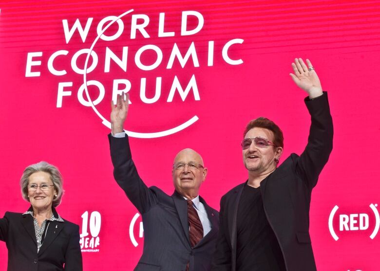 People stand and wave in front of a banner for the World Economic Forum.