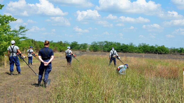 People sweep metal detectors across an open field.