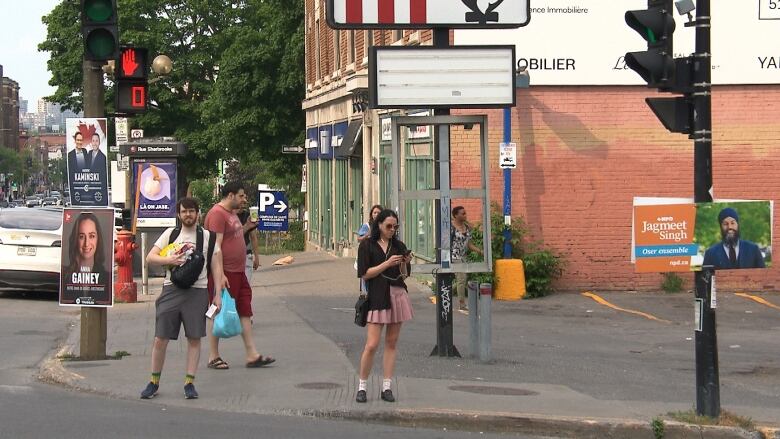 Pedestrians standing at a street light in NDG-Westmount, Montreal. They're surrounded by campaign signs 