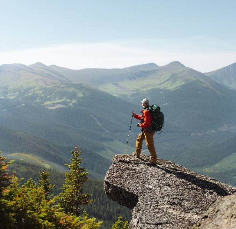 A hiker stands on a mountainous outcropping. 