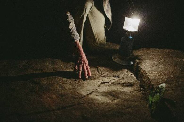 A light illuminates a dinosaur track while a person kneels above it. 