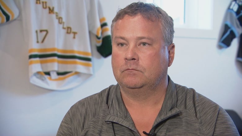 A man wearing a grey shirt sits in front of a hockey jersey with the words 