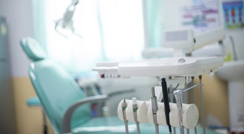 A stock photo shows dental instruments in the foreground with a light blue dentist's chair in a blurred background.