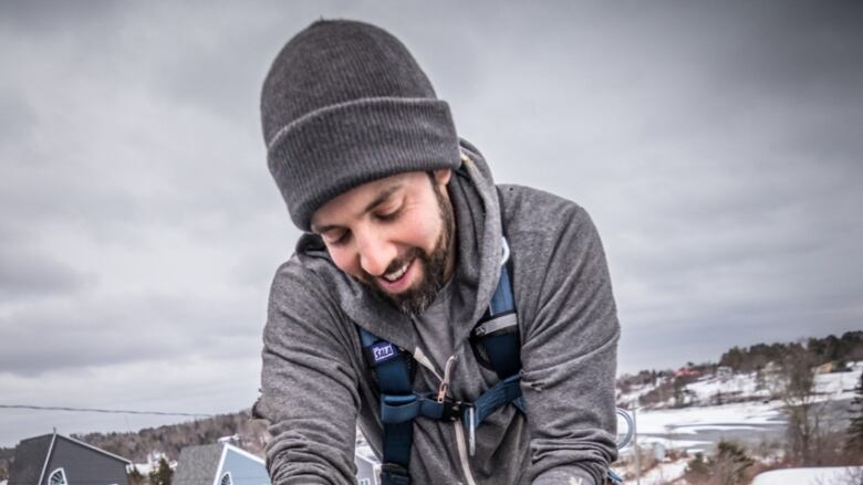 A man with a beard and a tuque is shown on a roof in winter installing solar panels.