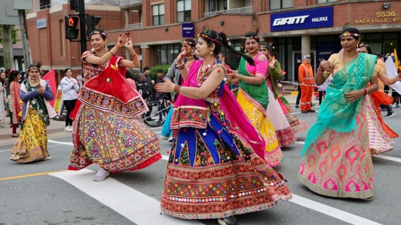 Dancers in bright Indian traditional clothes are shown on the street