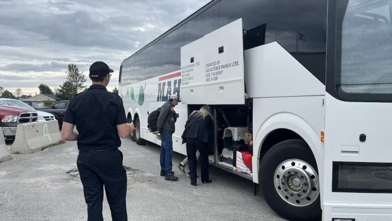 Three people load their belongings in a bus. 