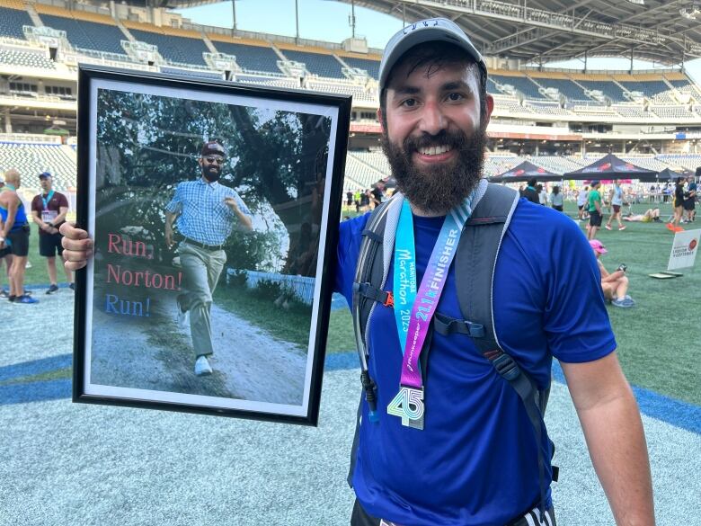 A man holds a framed photoshopped photo of his face on the body of Forrest Gump.