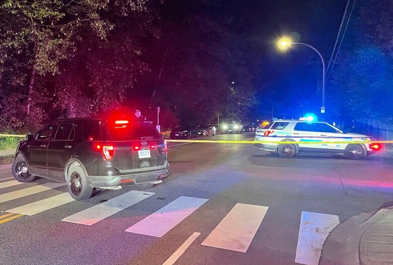 Two police vehicles with lights on and crime scene tape block access to a street at nighttime.