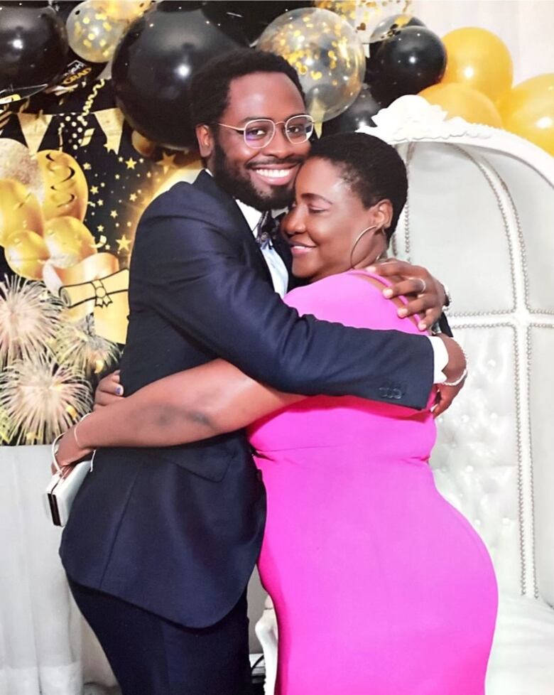 A young Black man hugging his mother in front of celebratory black and gold balloons.