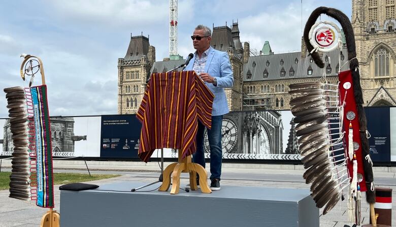 A man speaks at a podium with Parliament Hill's Centre Block in the background.