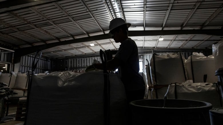 A man in shadow walks next to sacks filled with lithium carbonate. 